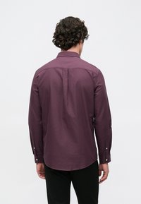 Hosszú ujjú, sötétlila gombos ing sima anyagból, hátulredővel és gombos mandzsettával, fekete nadrággal párosítva.