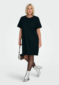 Czarna sukienka z krótkim rękawem o luźnym kroju. Noszona ze srebrnymi metalicznymi botkami za kostkę i trzymająca małą metaliczną torebkę.