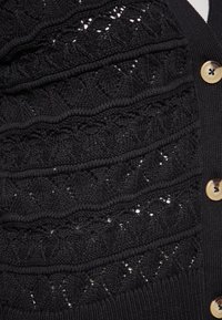 Cardigan nero a maglia con motivi testurizzati e fori decorativi. Bottoni dorati sul davanti, polsini e orlo a coste. Morbido, di peso medio.