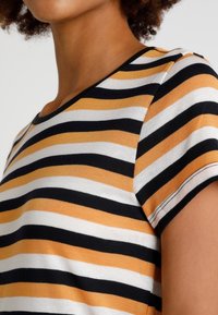 Triko s krátkým rukávem, které má černé, bílé a hořčičně žluté vodorovné pruhy, vyrobené z měkké bavlněné směsi s kulatým výstřihem.