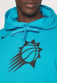 Felpa turchese con grafica di un pallone da basket nera e design a raggio di sole. Dotata di cappuccio con coulisse e stoffa morbida e testurizzata.