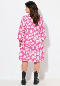 Rotes Kleid mit weißem abstraktem Muster, Dreiviertelärmel, gestufter Saum, kombiniert mit schwarzen Nieten-Stiefeletten. Glatte Stofftextur.