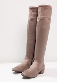 Knöchelhohe taupefarbene Wildlederstiefel mit quadratischen Zehen, einem leichten Blockabsatz und seitlichen Reißverschlüssen; glatte Textur mit subtilen Nähdetails.