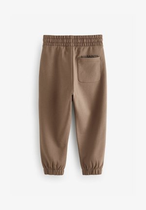 Bruna bomullsbyxor med elastisk midja, smalnande ben och en bakficka med texten "ALLSAINTS" i svart.