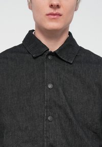 Svart denimjakke med kragehals, frontknapper og en teksturert finish, designet for en tettsittende passform.