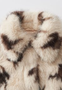 Fauxbonten jas met een beige en bruine gevlekte patroon, met een pluizige textuur en een brede kraag, die een zachte, luxueuze uitstraling biedt.