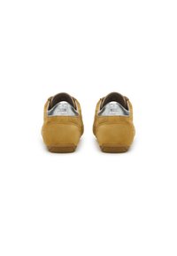 Sneakers gialli in suede con un tallone in argento, superficie texturizzata, forma arrotondata e suola in gomma marrone con un motivo a zigzag.