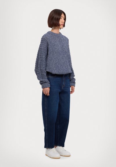 Jersey de punto grueso en color navy con textura acanalada, combinado con vaqueros azul de cintura alta y zapatillas blancas, presentando una silueta relajada.