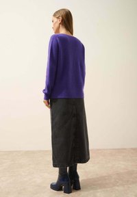 Fioletowy, strukturalny sweter z dzianiny zestawiony z długą czarną spódnicą dżinsową i niebieskimi botkami na obcasie, widok z tyłu. Prosta, nowoczesna sylwetka.
