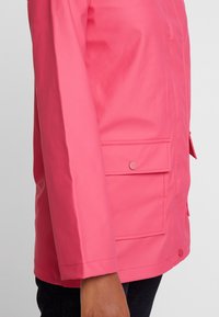 Vattentålig rosa jacka med rak skjortskärning, långa ärmar, framtill ficka med tryckknappsstängning och slät textur.