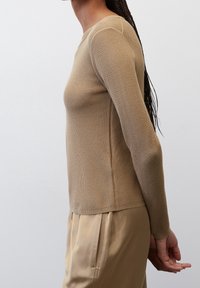 Beige, geribbelde top met lange mouwen en een aangesloten silhouet. Heeft een textuurstof, ronde halslijn en verlengde mouwen, gecombineerd met lichte broeken.