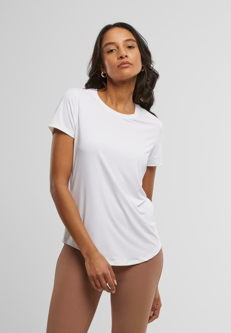 Witte t-shirt met korte mouwen in een zachte, lichte stof, voorzien van een ronde halslijn en een gebogen zoom, gecombineerd met strakke, bruine leggings.