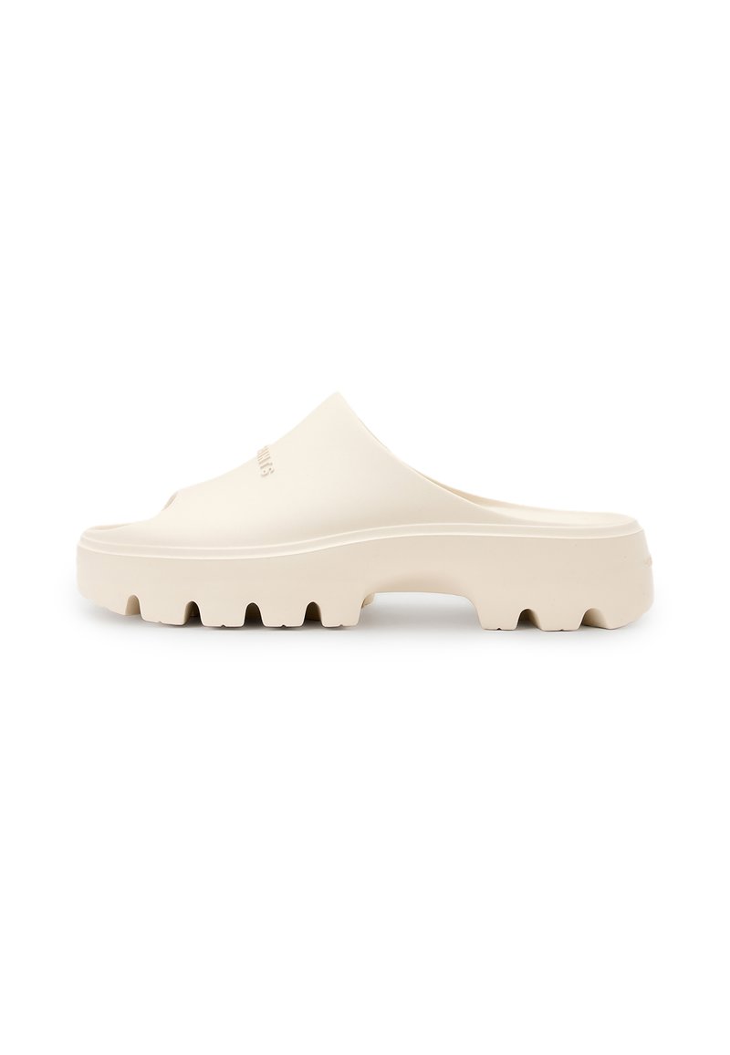 Beige slide sandal with a smooth upper and thick, textured sole featuring deep grooves for traction. Simple, minimalist design.