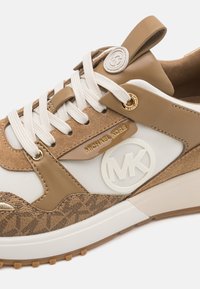 Michael Kors joggesko med beige semsket skinn og mesh-overdel, hvite accenter, rund logo og teksturert detaljer på sålen.