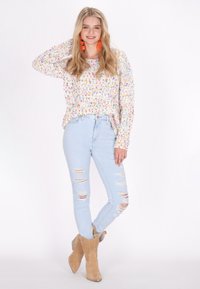 Kleurrijke gemêleerde gebreide trui, lichte denim skinny jeans met gescheurde accenten en beige enkellaarsjes. Zachte textuur en losse pasvorm.