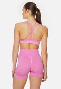 Roze sportbh met kruisbanden op de rug, gecombineerd met bijpassende hoge shorts. Soepele textuur, minimale patroon details aan de randen.
