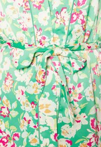 Sukienka w kwiaty z zielonym tłem, białymi i różowymi kwiatami, z paskiem wiązanym w talii oraz miękkim, teksturowanym materiałem.