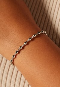 Zilveren kralenarmband om een bruine pols, met afwisselend gladde en getextureerde ronde kralen in een slank, flexibel ontwerp.