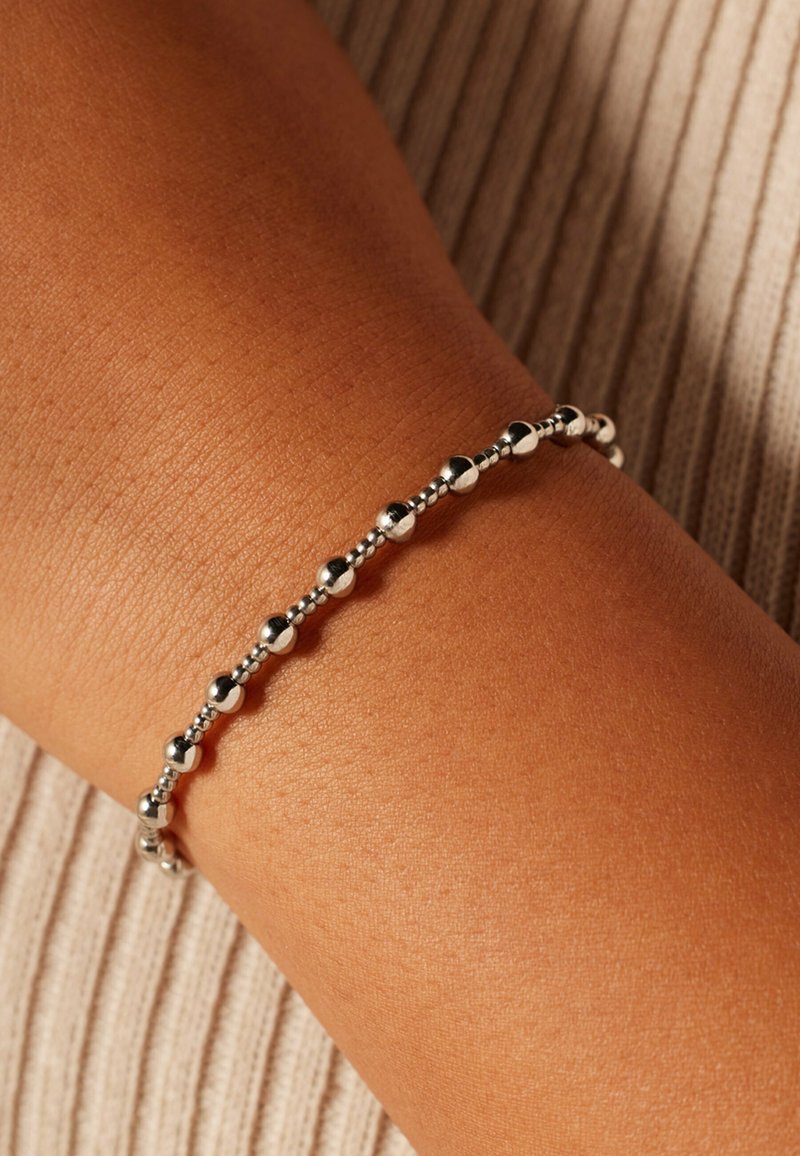 Zilveren kralenarmband om een bruine pols, met afwisselend gladde en getextureerde ronde kralen in een slank, flexibel ontwerp.