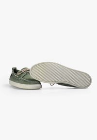Scarpe da barca in pelle verde con suola in gomma bianca, dettagli di cucitura e accenti in pizzo. Presentano una superficie liscia e un design a punta rotonda.