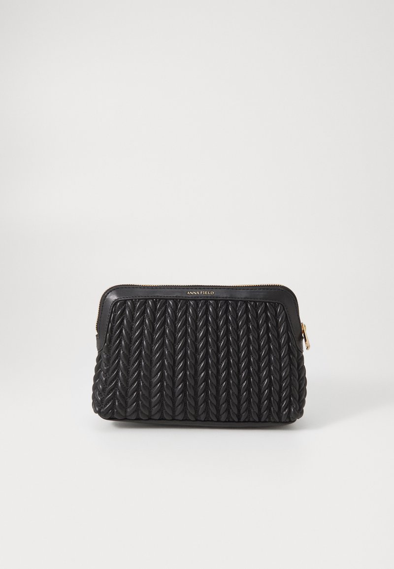 Clutch de cuero negro con textura trenzada, con un zipper dorado y un logo en la parte superior. Forma rectangular compacta, con costuras decorativas.