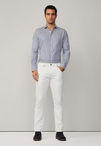 White jeans paired with a blue and white striped button-up shirt. The shirt has long sleeves and a classic collar. Footwear includes dark boots.