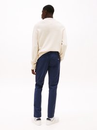 Béžový sveter s textúrovaným pletením, skombinovaný s námorníckymi modrými slim-fit nohavicami. Model má na sebe biele tenisky s čiernymi akcentami.