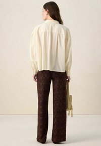 Cream-colored, oversized shirt with button cuffs paired with wide-leg brown pants featuring a textured shell pattern.