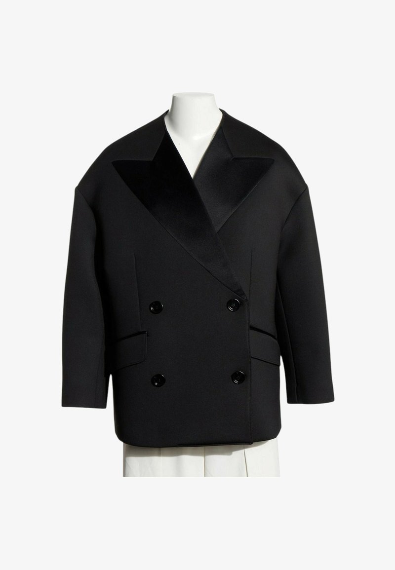 Blazer noir croisé avec larges revers en satin, deux poches avant à rabat et manches trois quarts sur un mannequin blanc.