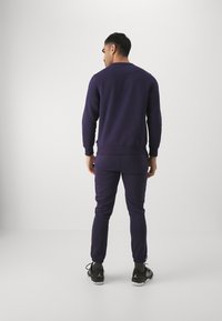 Sudadera de color púrpura marino y pantalones de chándal a juego, fabricados en un tejido suave, con un diseño sencillo que incluye puños acanalados y tobillos elasticados.