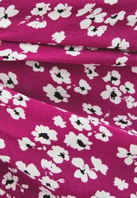 Klart rosa tyg med vitt blommönster som har små svarta detaljer, visad i mjuka veck och närbild.