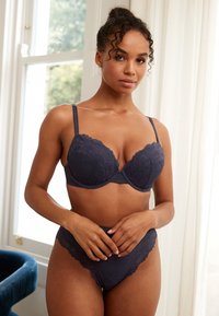 Soutien-gorge marine doublé de dentelle avec bonnets rembourrés et bretelles réglables, assorti à une culotte taille haute style bikini avec bord festonné.