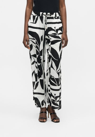 Personne portant un pantalon large noir et blanc avec des motifs abstraits de feuilles et des sandales noires à talons hauts avec brides.