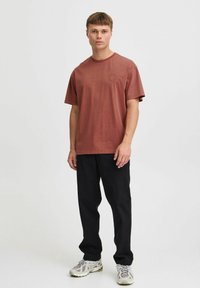 Rustfaret kortærmet T-shirt i bomuld med rund halsudskæring, prydet med en diskret logo-detalje. Samlet med sorte bukser og sneakers.