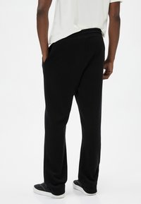 Pantalones de chándal negros con corte relajado, hechos de una tela suave. Cuentan con una cinturilla elástica y bolsillos laterales. Combinados con zapatillas negras.