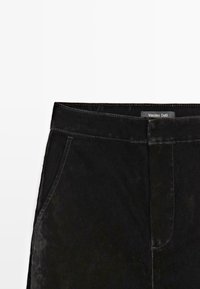 Pantalon en velours noir avec poches latérales et ceinture, présentant des coutures discrètes et une étiquette Massimo Dutti visible.