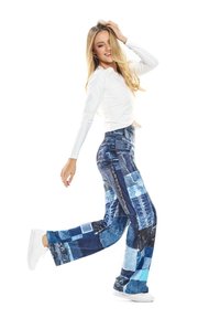 Top blanco ajustado de manga larga combinado con pantalones de mezclilla azul que presentan distintos patrones de patchwork. Los pantalones tienen una pierna recta y un ligero brillo.
