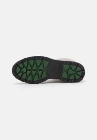 Sola della scarpa con una base nera e un motivo di trazione in gomma verde. Presenta lugs triangolari e un marchio centrale.