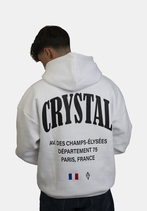Felpa bianca con grande testo nero "CRYSTAL" sul retro, che include un indirizzo di Parigi e un dettaglio della bandiera francese. Materiale in cotone, vestibilità rilassata, design con cappuccio.