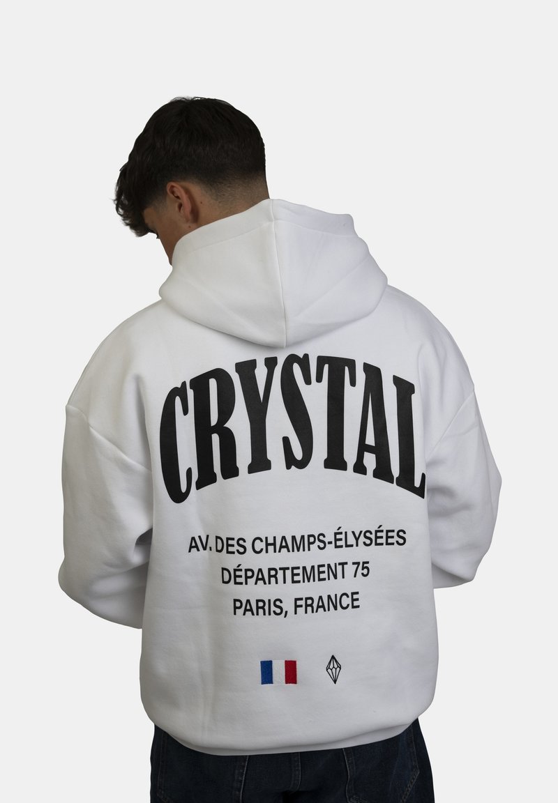 Felpa bianca con grande testo nero "CRYSTAL" sul retro, che include un indirizzo di Parigi e un dettaglio della bandiera francese. Materiale in cotone, vestibilità rilassata, design con cappuccio.