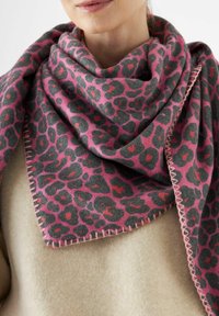 Femme portant une écharpe en imprimé léopard rose foncé et gris enroulée autour de son cou sur un pull beige, visage partiellement visible.