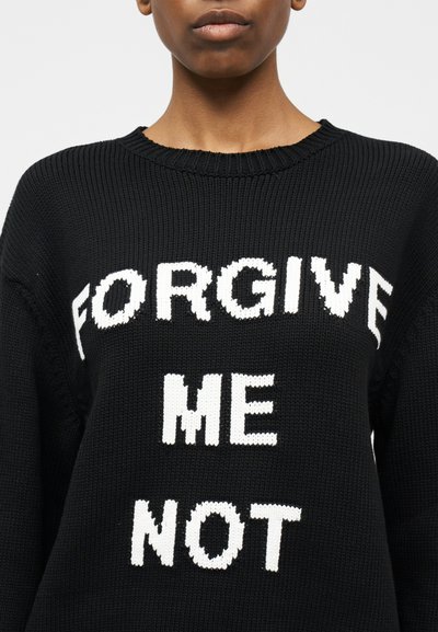 Άτομο που φοράει μαύρο πλεκτό πουλόβερ με λευκή επιγραφή που λέει «ΜΗ ΜΟΥ ΣΥΓΧΩΡΕΙΣ» στο μπροστινό μέρος.