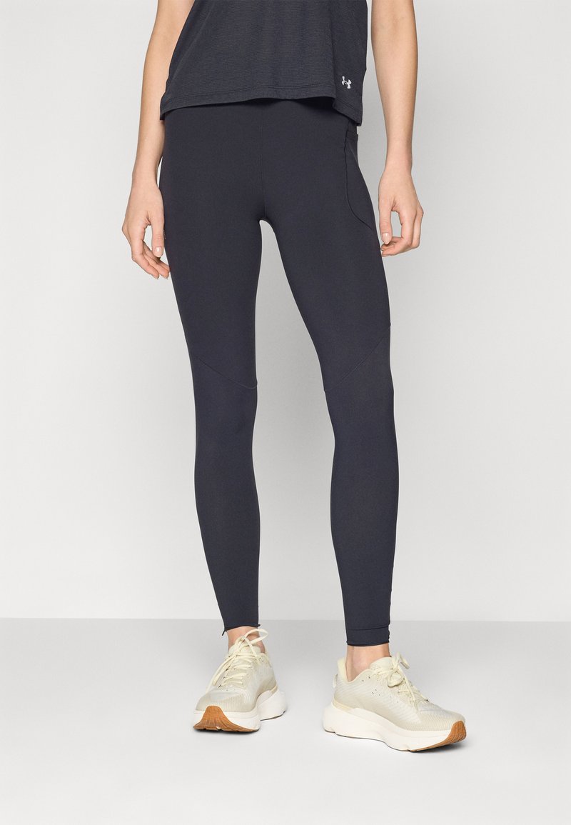 Fekete sport leggings, testhez simuló fazonban, sima textúrával és varrási részletezéssel, világos színű sportcipővel és sötét felsővel párosítva.