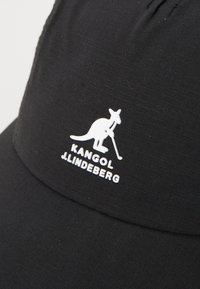 Μαύρο καπέλο φτιαγμένο από υφασμάτινη υφή με λευκό λογότυπο καγκουρό και κείμενο επωνυμίας. Ο σχεδιασμός περιλαμβάνει έναν καμπυλωτό γείσο και δομημένο θρόισμα.