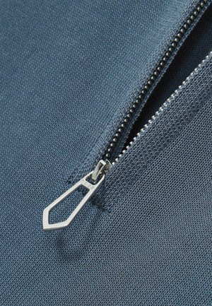 Țesătură albastră cu un fermoar, având un tab de metal la începutul fermoarului și dantură expusă. Textura este netedă, cu un model de țesătură subtil.