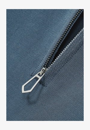 Sinine kangas, millel on tõmblukk, millel on metallist tõmbluku tõukur ja avatud hambad. Tekstuur on sile, peene kude mustriga.