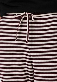 Bordowo-kremowe spodnie do noszenia w domu w paski z teksturowanej tkaniny. Posiadają ściągacz w pasie z sznurkiem oraz elastyczną gumkę dla wygody.