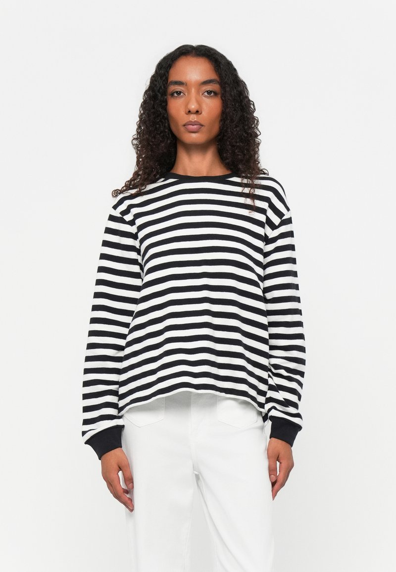 Zwart-witte gestreepte langemouwen shirt met een ronde hals en elastische manchetten, gedragen over witte broek. Heeft een relaxte pasvorm en een zachte textuur.