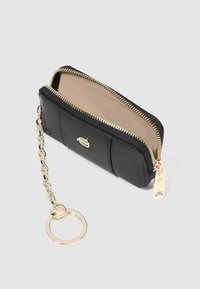 Portafoglio in pelle nera con cerniera dorata, attacco a catena e anello circolare; presenta un interno beige e un design strutturato.