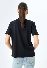 Sort bomulds-t-shirt med kortærmet design, let oversized pasform og rund halsudskæring, parret med lyseblå jeans.